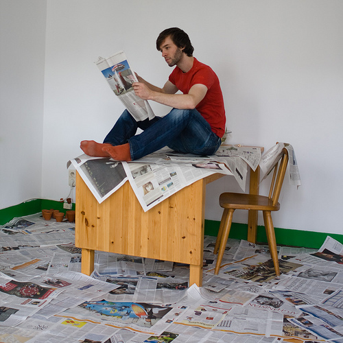 Reading the newspaper on a table surrounded by newspapers